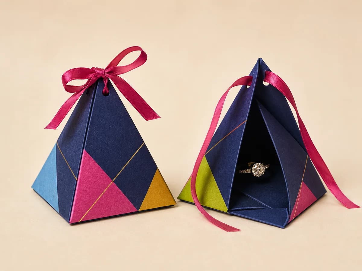Navy pyramid-shaped jewellery favour boxes with pink ribbon bows, one open showing a ring