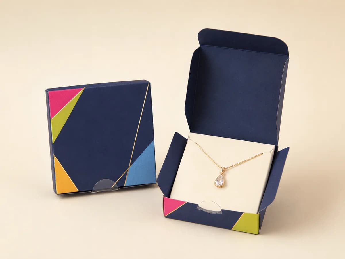Shallow navy tuck-lock necklace box open to show a gold pendant necklace on a cream insert card
